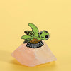 A cute sea turtle enamel lapel pin brooch with green and brown coloring resting on a pink stone.