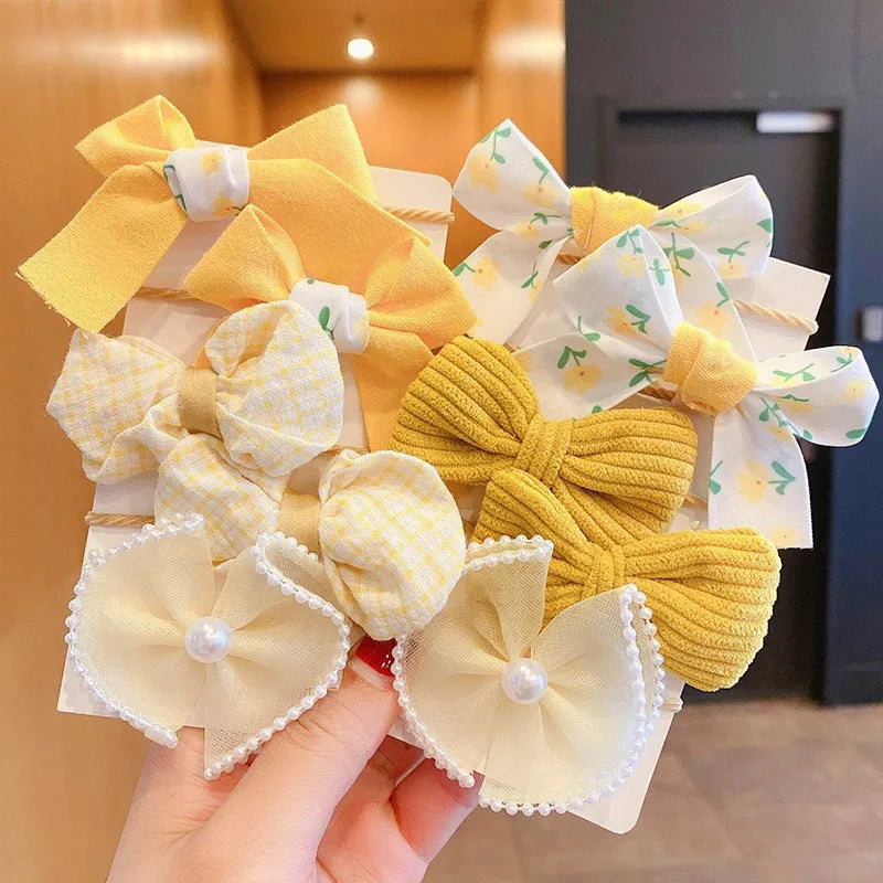 A hand holds a cluster of yellow and white fabric flower bow hair ties.