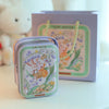 A decorative tinplate candy box with a carrying loop featuring floral designs and a light purple background.