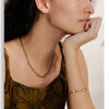 A close-up of a woman wearing a gold stainless steel charm necklace and a gold bracelet.