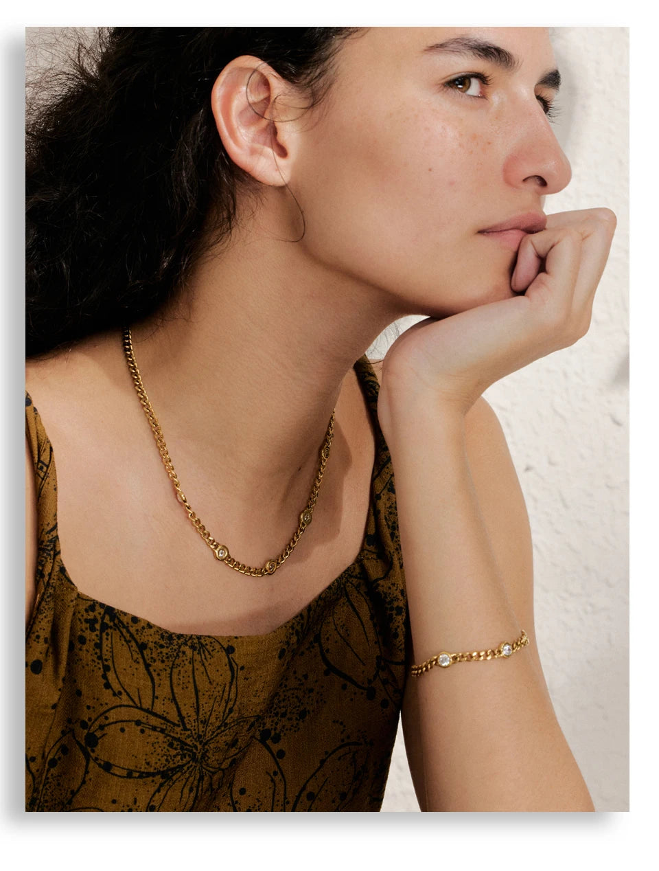 A close-up of a woman wearing a gold stainless steel charm necklace and a gold bracelet.
