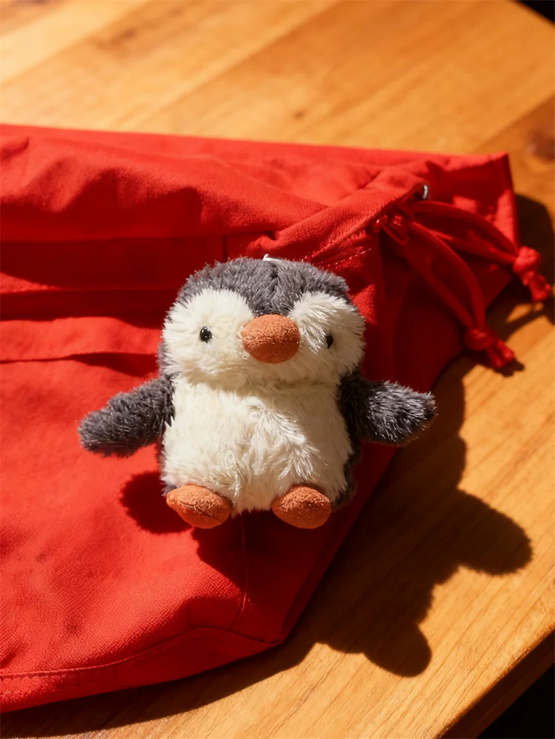 Peluche de pingüino gris y blanco esponjoso dentro de una funda protectora de tela roja.