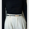 A close-up shot of a woman wearing a white pleated skirt and a black top with a gold buckle skinny leather belt.