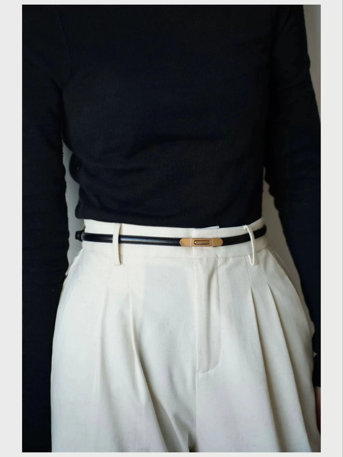 A close-up shot of a woman wearing a white pleated skirt and a black top with a gold buckle skinny leather belt.