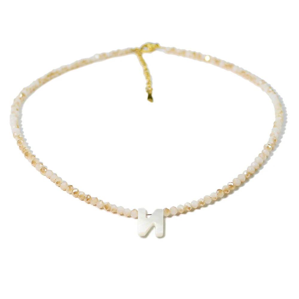 A delicate necklace made of mother of pearl beads with crystal accents, featuring a silver initial charm.
