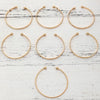 A set of eight elegant gold hexagon star twist bangles arranged in a grid on a white wooden surface.