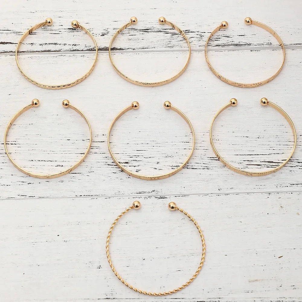 A set of eight elegant gold hexagon star twist bangles arranged in a grid on a white wooden surface.