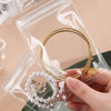 A hand holds a gold hoop earring inside a clear self-sealing jewelry storage pouch.