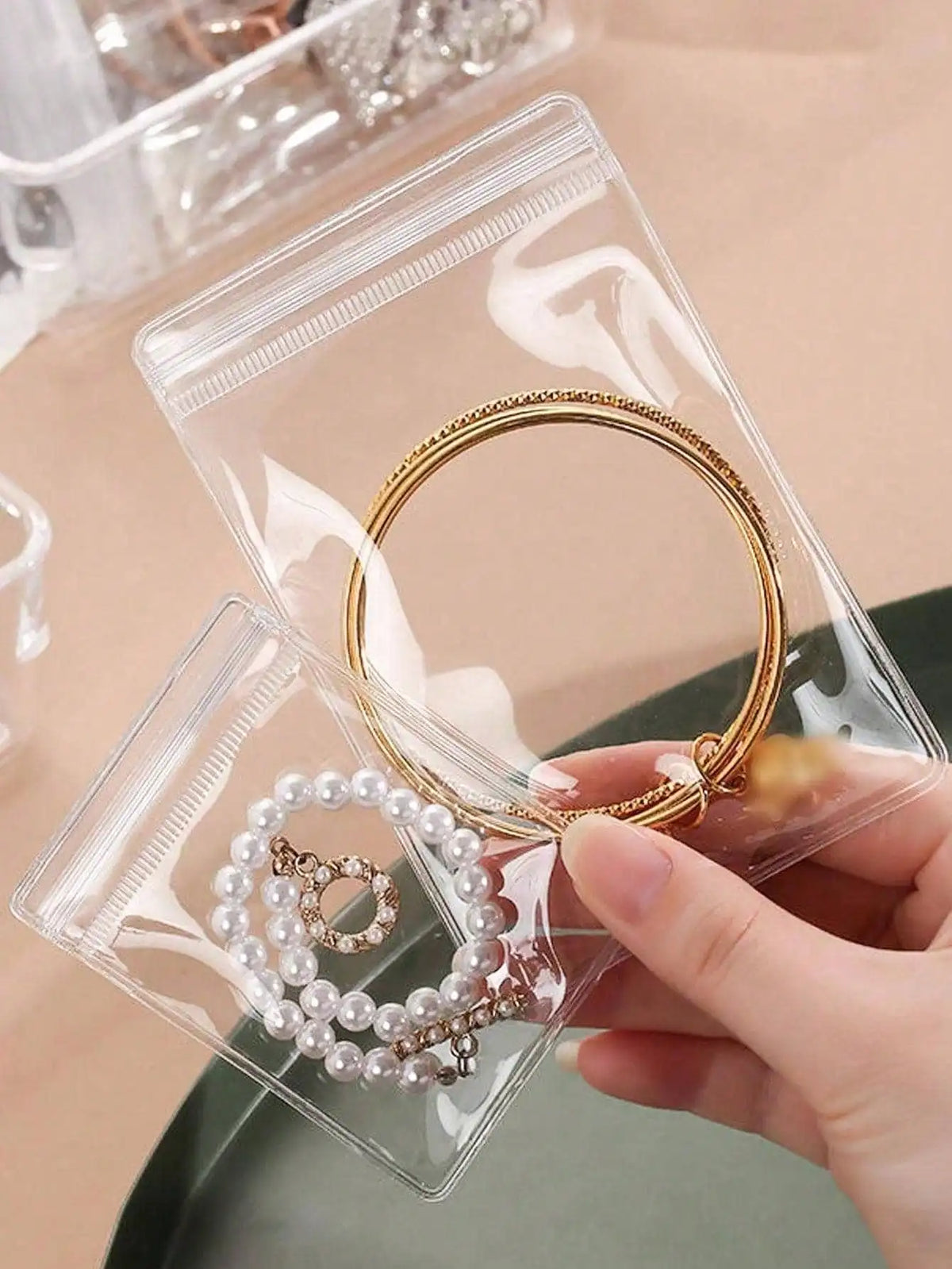 A hand holds a gold hoop earring inside a clear self-sealing jewelry storage pouch.