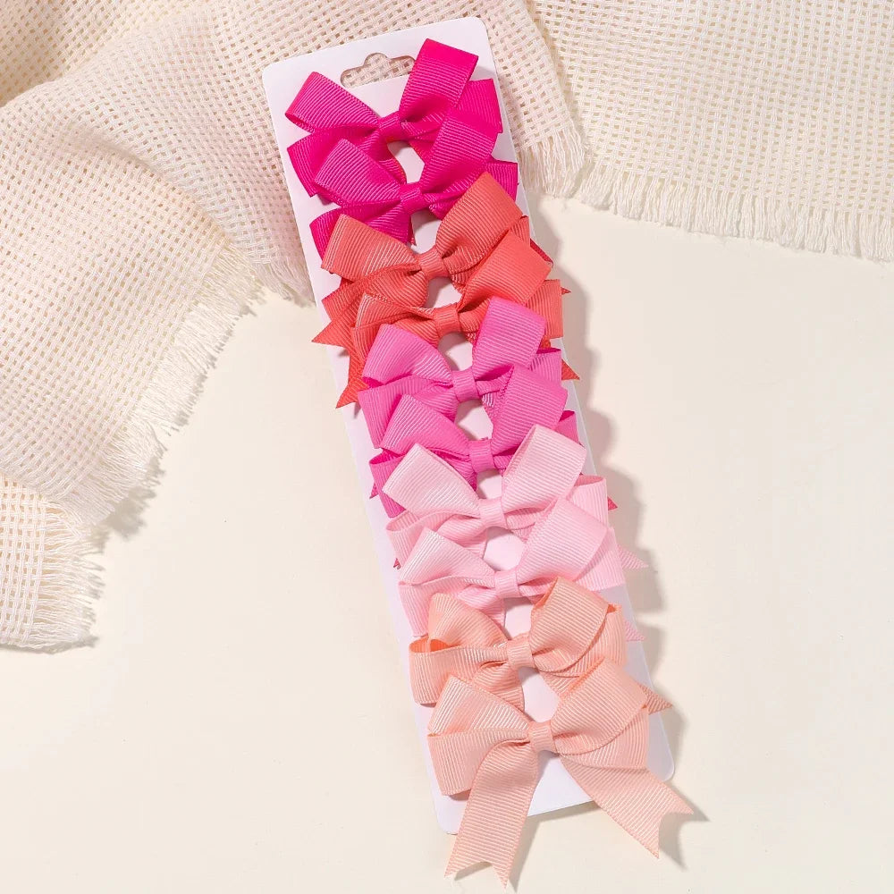 A display of pink and coral handmade ribbon bow hair clips arranged in a vertical row on a white card.