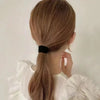 A woman ties her hair into a ponytail using a black elastic band against a light background.