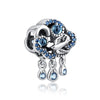A silver family tree charm featuring a bird and blue gemstones with dangling teardrop charms.