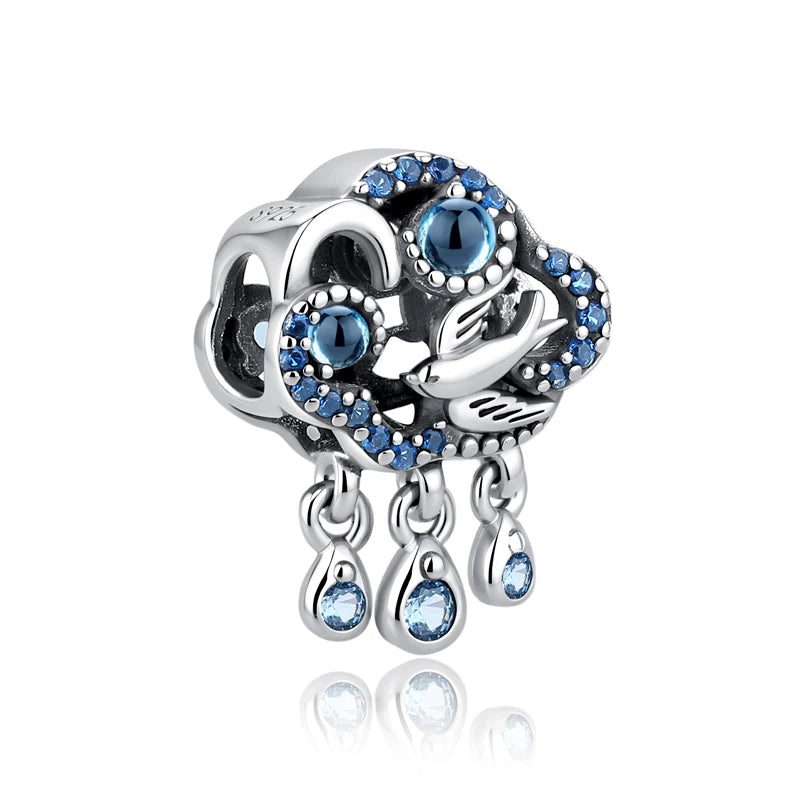 A silver family tree charm featuring a bird and blue gemstones with dangling teardrop charms.