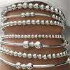 A collection of silver minimalist round beaded bracelets stacked on a person's wrist.