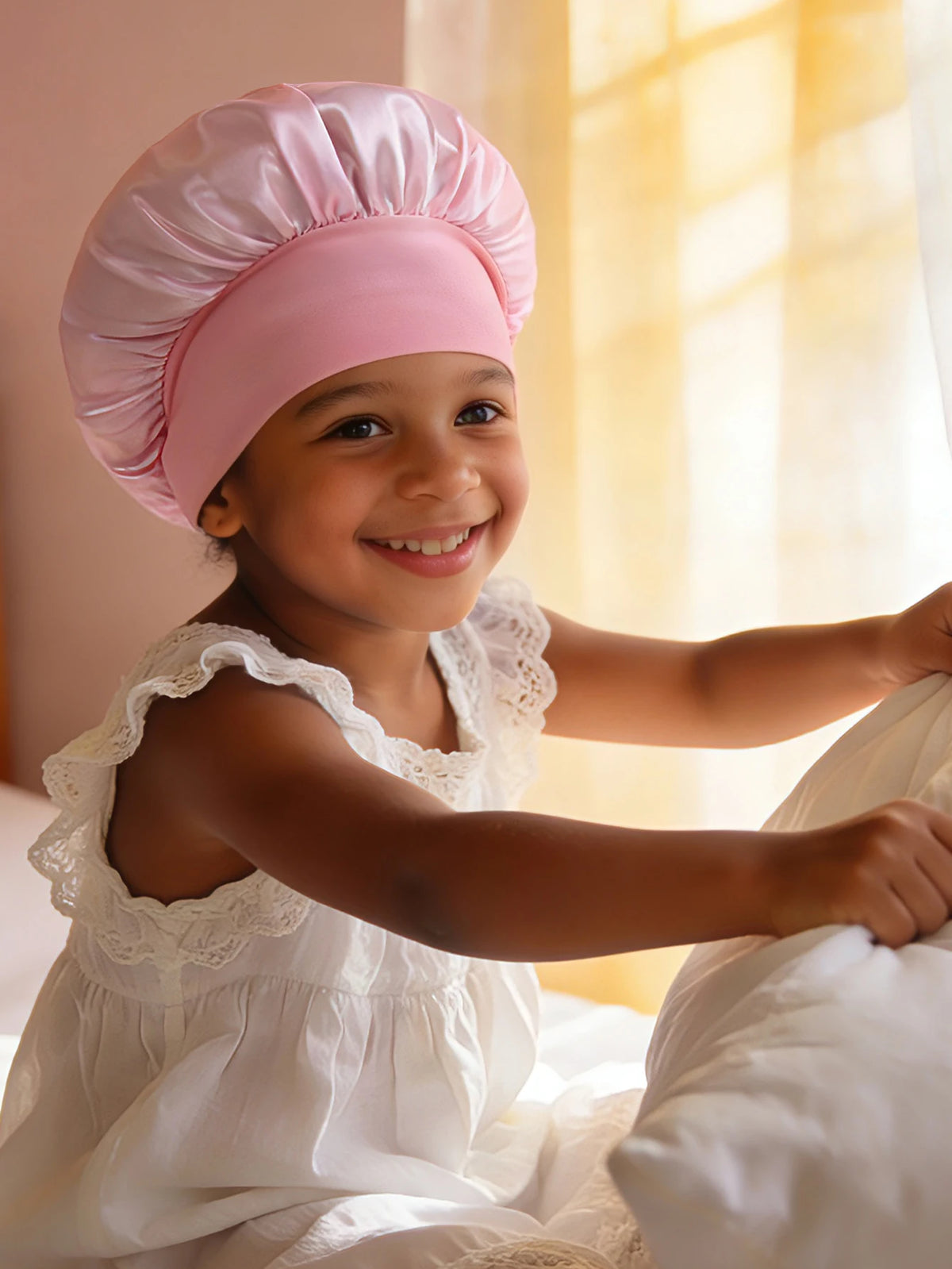 A smiling young girl wearing a pink A-Z letter sleep cap while sitting near a window.