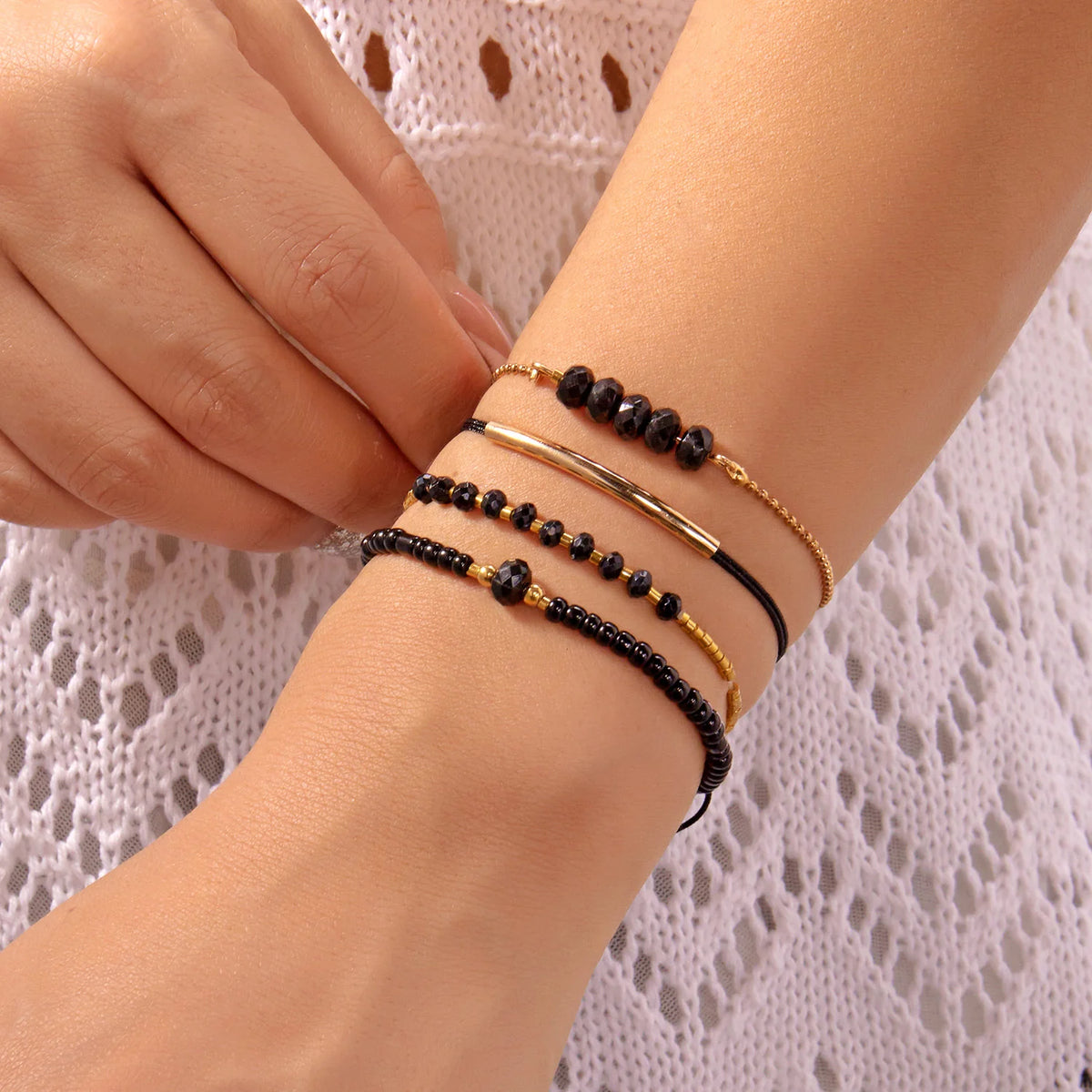 A close-up of a hand wearing a stack of black and gold beaded bracelets on the wrist.