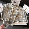 A beige and gold patterned silk scarf draped on a white card against a dark background.