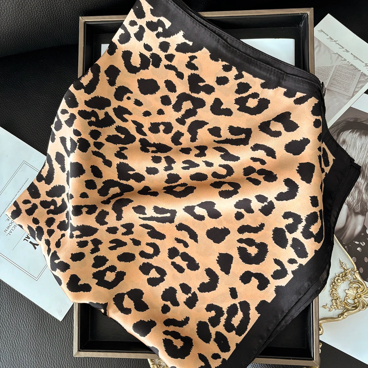 A luxury leopard print silk scarf in black and tan is displayed in a wooden frame.