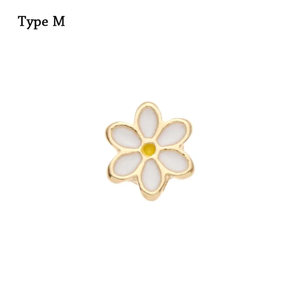 Un pequeño adorno de pulsera de metal con forma de flor, centro blanco y acento amarillo.