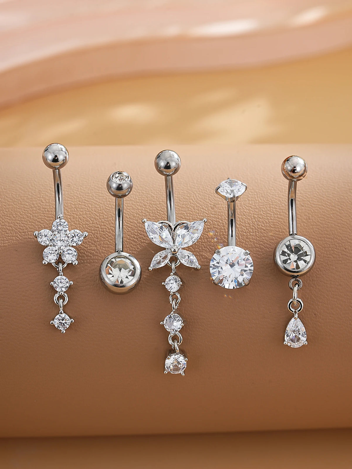 A set of five gold stainless steel dangled belly button rings featuring various diamond and gemstone designs.