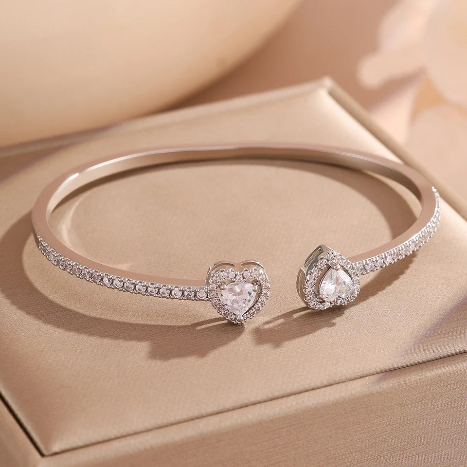 A set of geometric rhinestone heart stacking bracelets displayed on a light beige box.