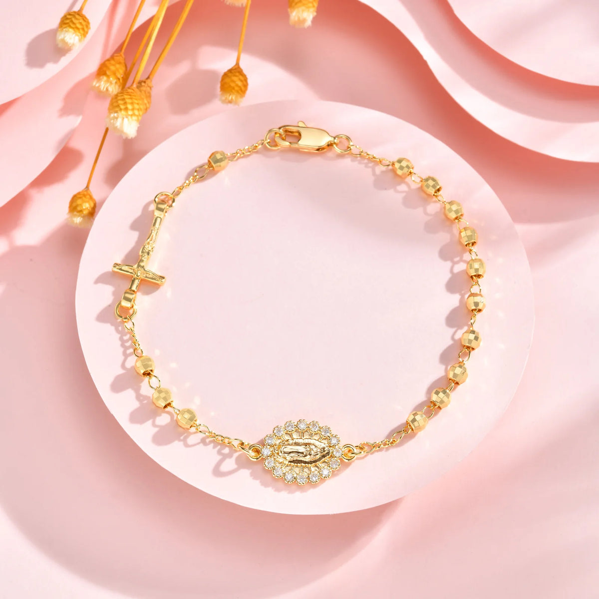 A delicate 18K gold plated rosary bracelet for women displayed on a pink background.