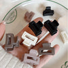A hand holds a set of twelve rectangular hair clips in various shades of black, brown, and white.