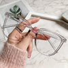 A hand holds a pair of clear, large square anti-blue light spectacles against a marble background.