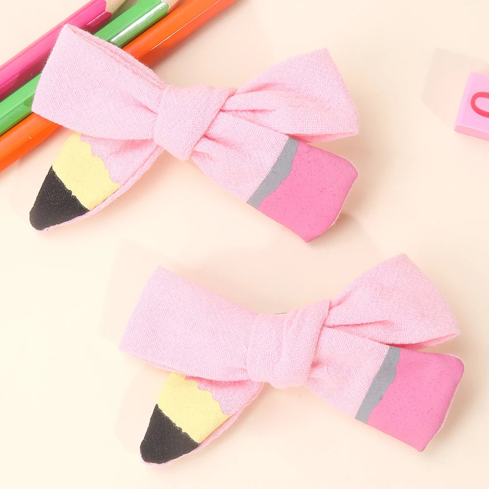 A pink bow hair clip made of felt with yellow and black accents, shown next to colored pencils.