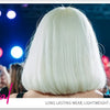 A person with long white hair is featured in a concert setting, facing away from the camera.