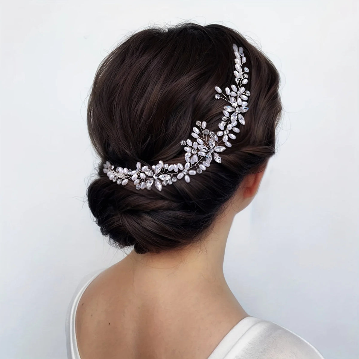 A dark brown updo hairstyle featuring a delicate silver rhinestone bridal headband woven into the hair.