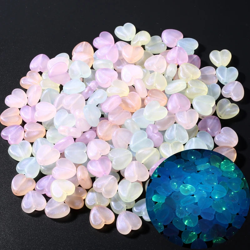 A collection of translucent pink and white glow-in-the-dark acrylic heart-shaped beads next to a sphere of bright blue glow-i