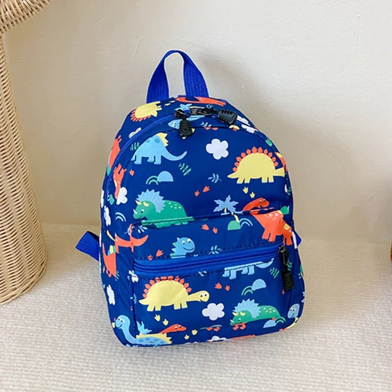 A blue kids backpack featuring a cute dinosaur and unicorn pattern, resting on a white surface.