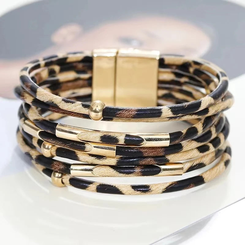 Une pile de bracelets de perles en cuir léopard bohèmes avec accents dorés, exposés sur une surface blanche.