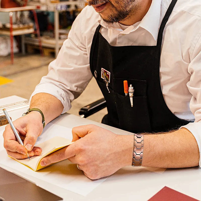 A person in an apron is writing on paper, holding a copper magnetic therapy bracelet.
