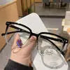 A hand is holding clear anti-blue light glasses with black frames on a white surface.