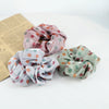 Three colorful knitted fabric scrunchie headbands in shades of pink, green, and lavender are displayed next to a piece of pap