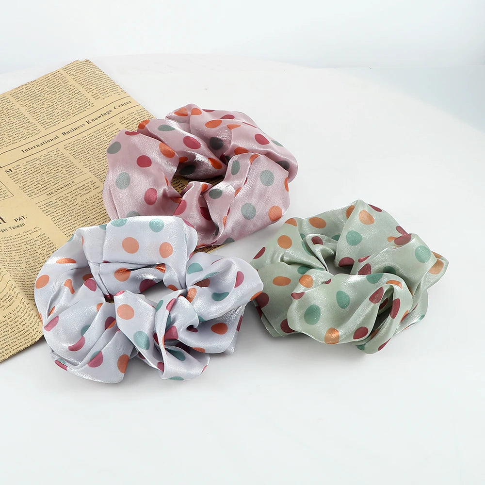Three colorful knitted fabric scrunchie headbands in shades of pink, green, and lavender are displayed next to a piece of pap