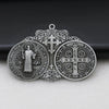 A silver Saint Benedict protection medal featuring a cross and various religious symbols, displayed on a dark surface.