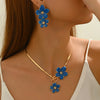 A woman wearing a gold floral pendant necklace and matching earrings with blue flowers.