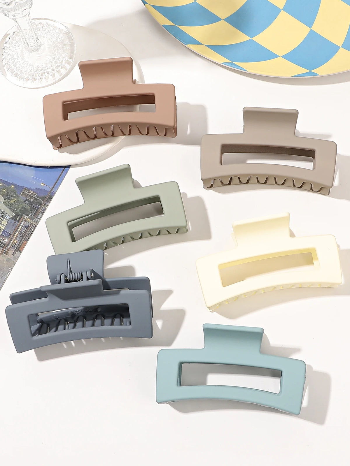 A set of seven square hair claw clips in various muted tones, including beige, gray, and blue-green.