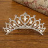 A sparkling crystal princess tiara hair comb adorned with pearls resting on a wooden surface.