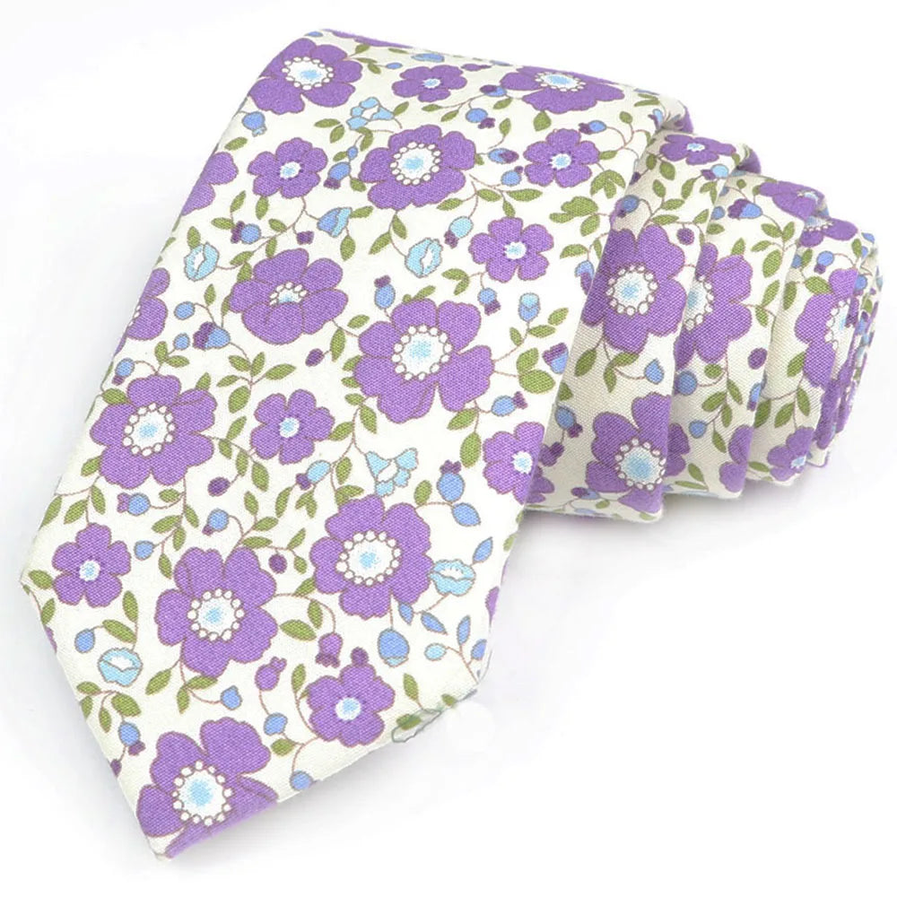Une pile de nœuds à col en coton à imprimé floral élégant avec des fleurs violettes et vertes sur fond blanc.