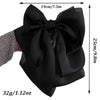Black satin bow hair clip shown with dimensions and a hand for scale.