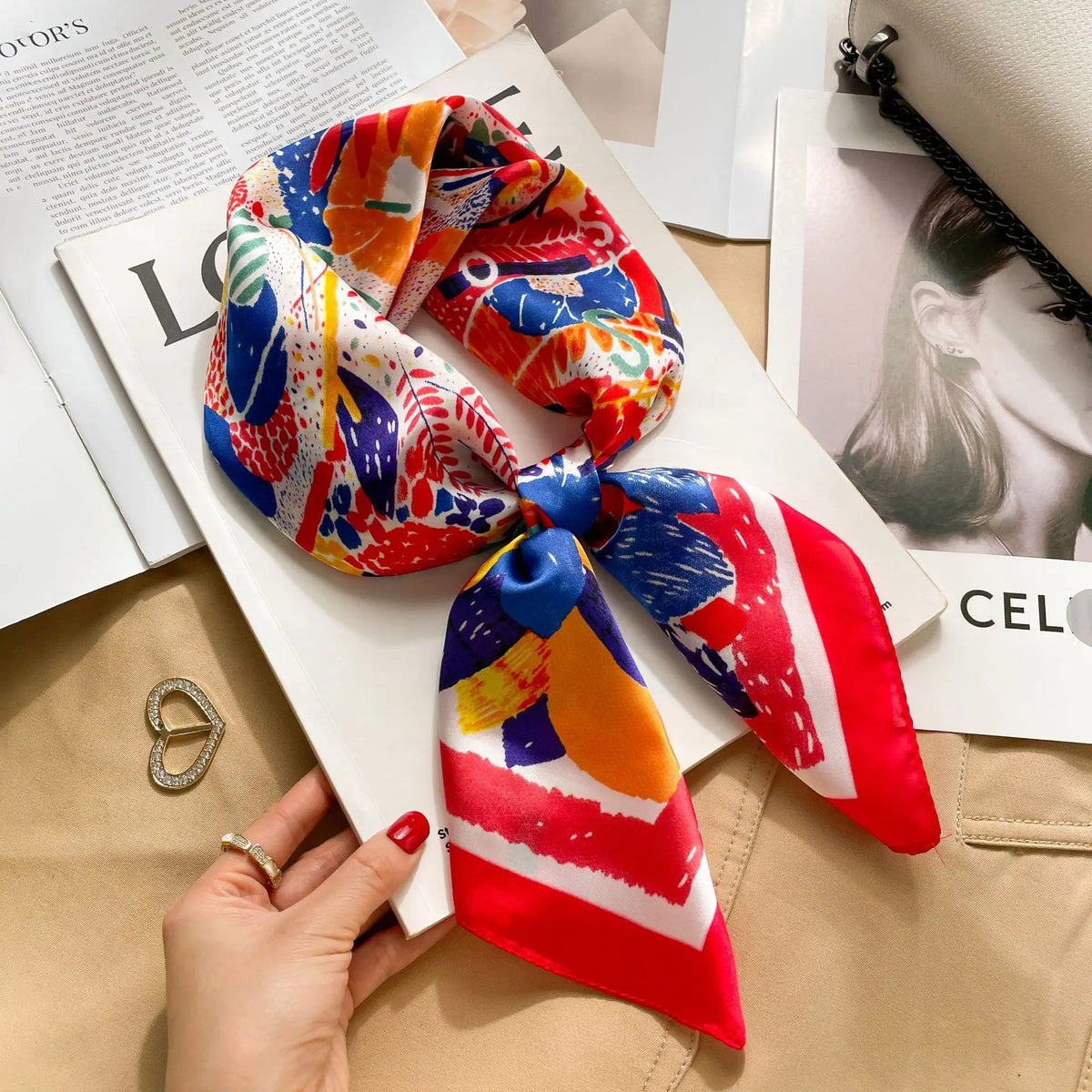 A vibrant silk scarf featuring abstract floral patterns in red, blue, orange, and white is displayed on a white card.