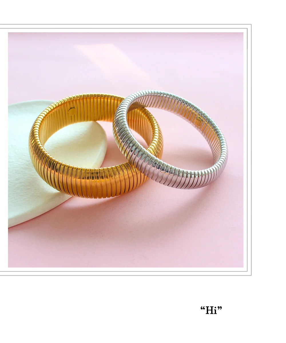 Two stacked gold and silver stainless steel elastic bangle bracelets on a pink background