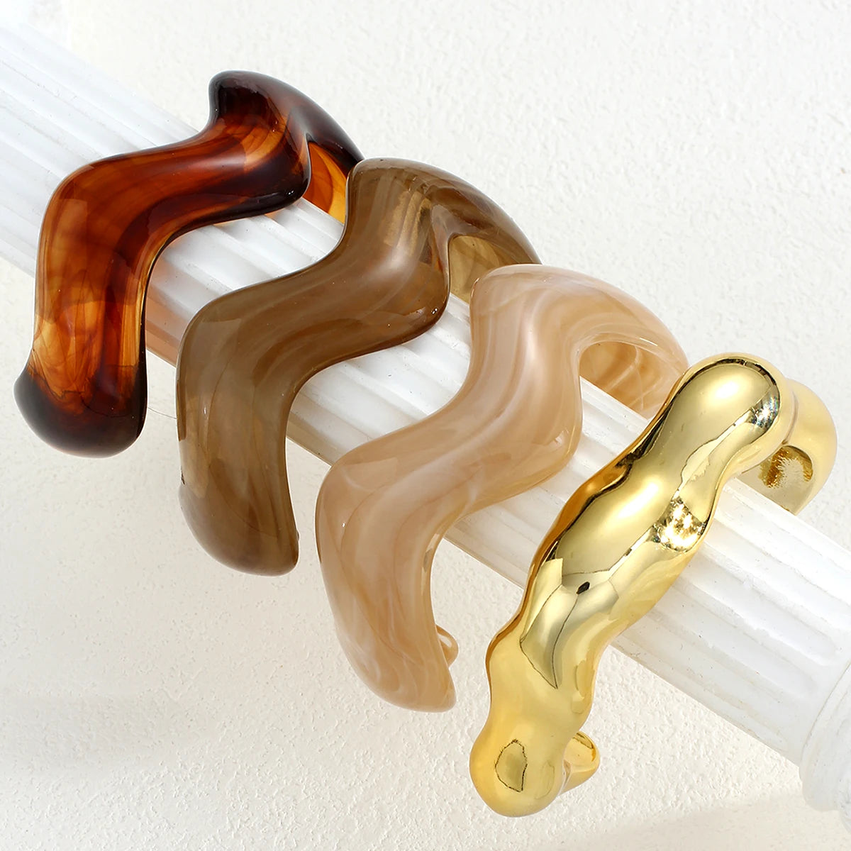A set of vintage minimalist wavy bangle bracelets in shades of amber and gold displayed on a white stand.