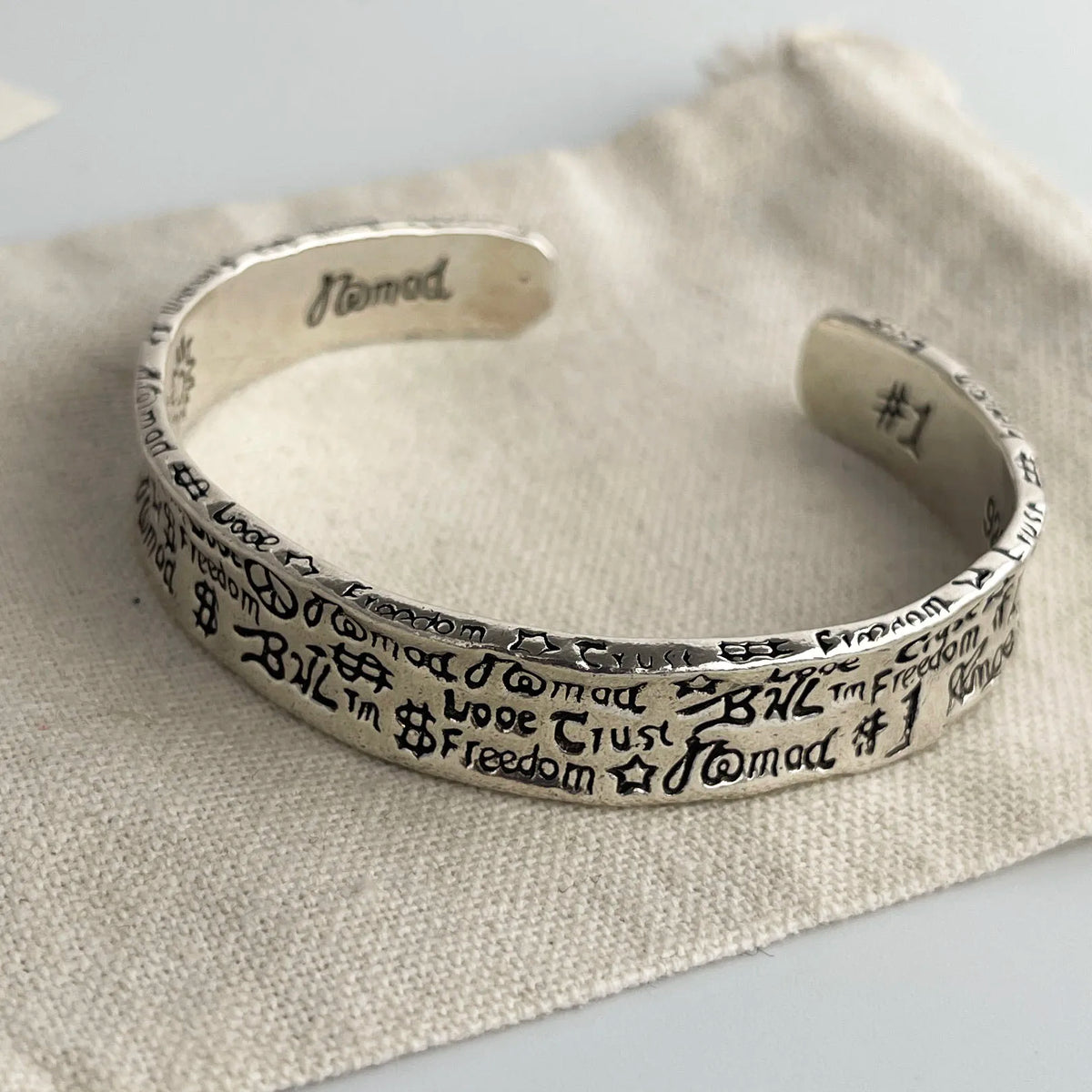 A sterling silver charm bracelet with various engraved charms resting on a beige linen fabric.