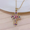 A gold-toned vintage cross pendant necklace featuring pink and blue gemstones on a white background.