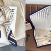 A beige blazer with a navy and white striped silk scarf draped over it, next to a folded white card.
